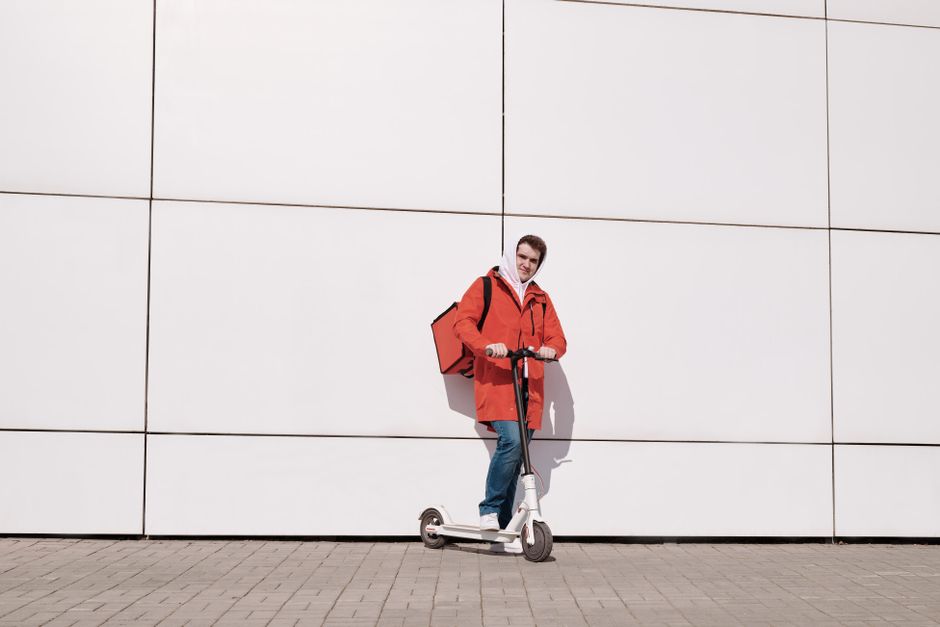 Man in red jacket with thermal bag on scooter, urban delivery service.